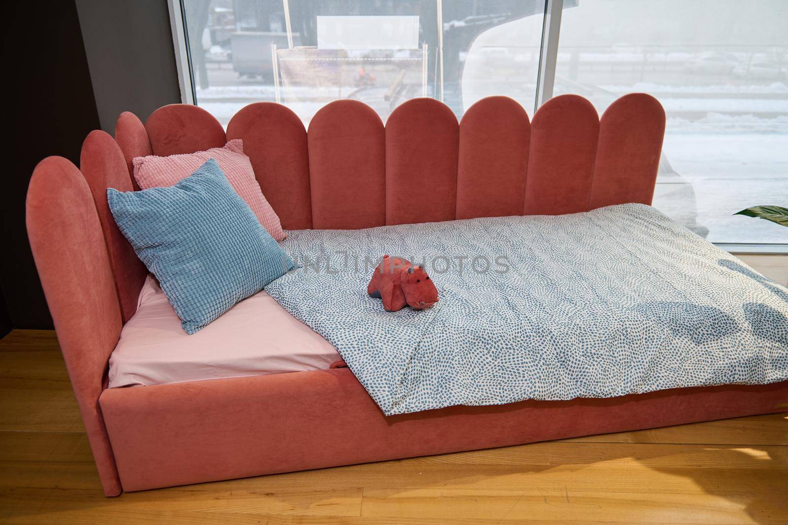 Modern stylish and minimalist children's sofa bed with soft bright coral velour fabric, on display for sale in the showroom of the highest quality furniture store
