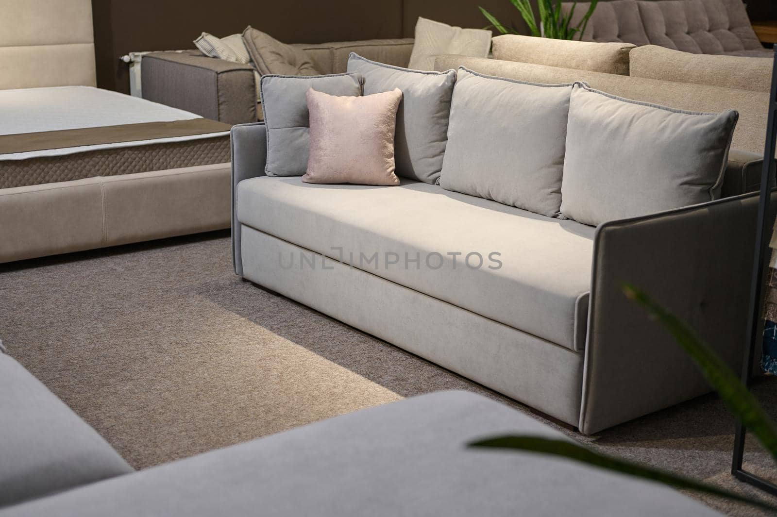 Exposition of upholstered modern comfortable light gray settee with pink cushions near a stand with swatches and fabric samples of different textures and qualities. Furniture store showroom by artgf