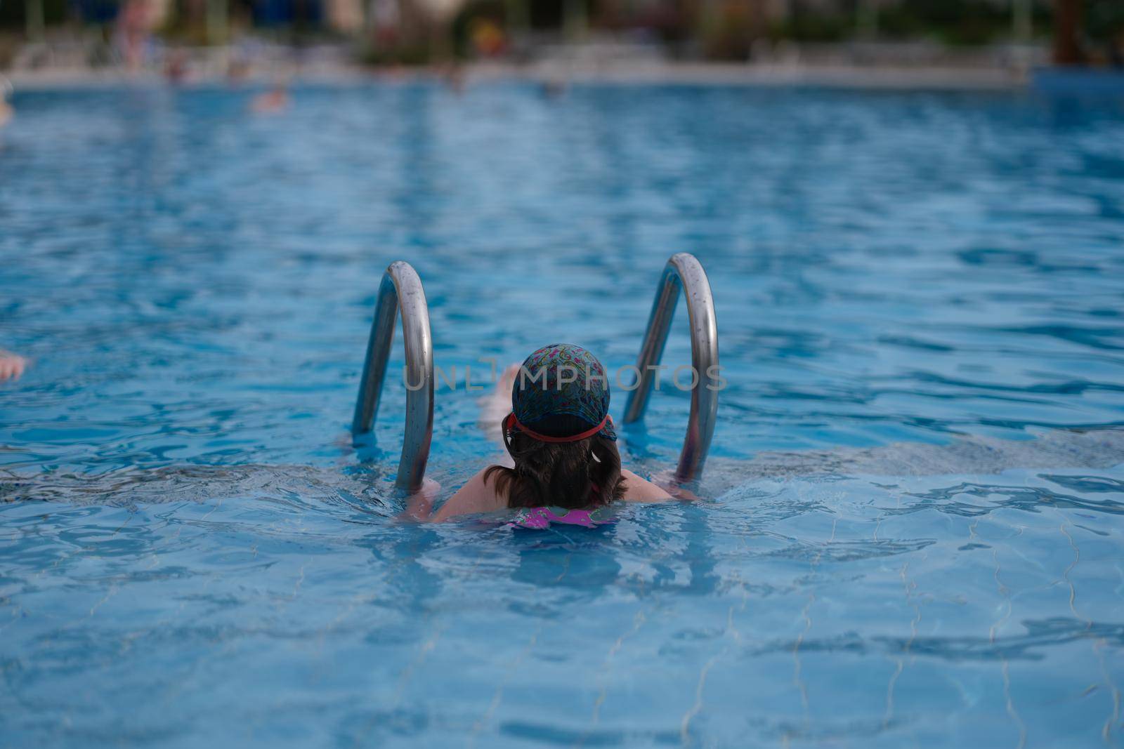 Little girl swimming in pool on vacation back view. Swimming lessons for children concept