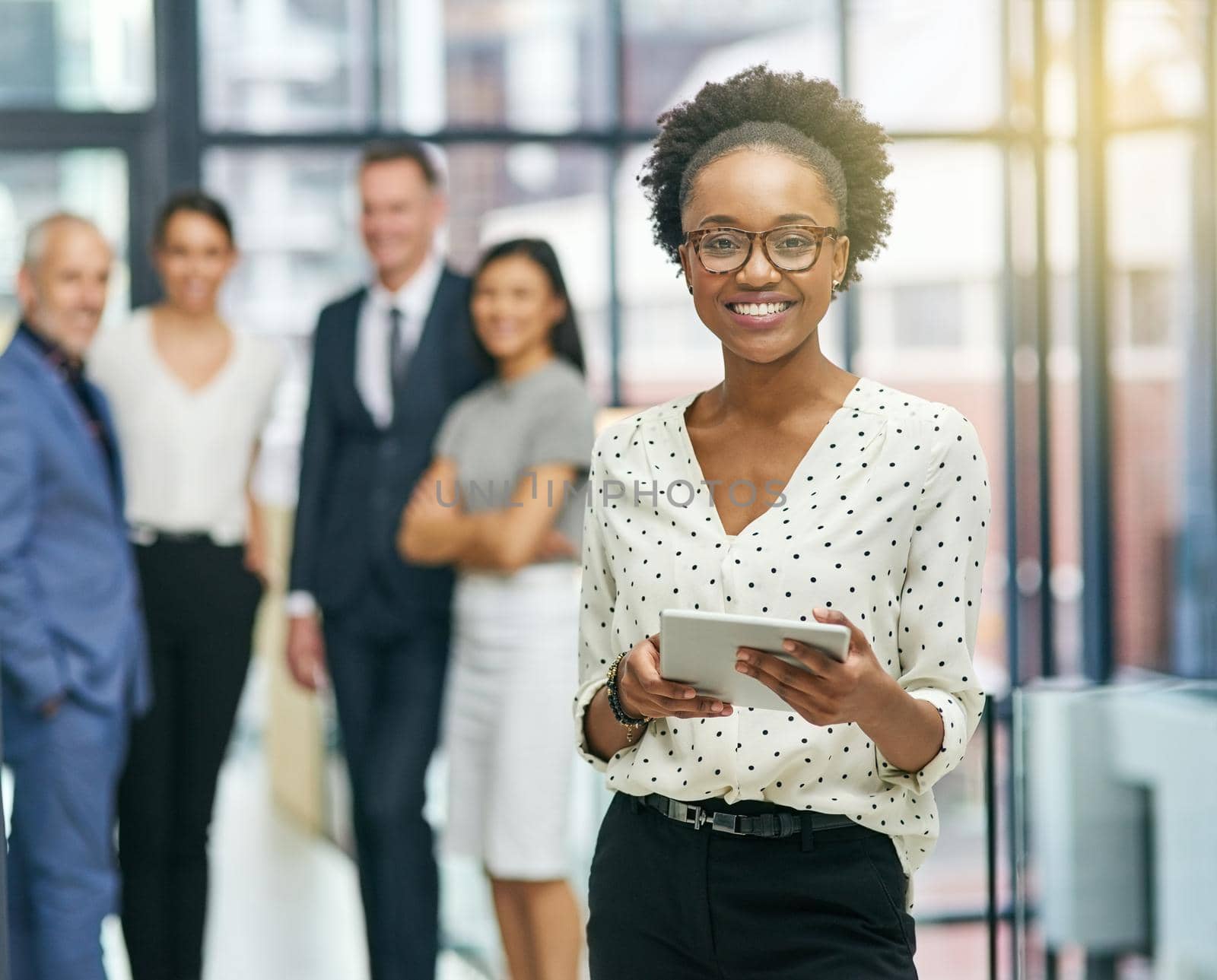 Portrait of a young businesswoman holding a digital tablet with her colleagues in the background.