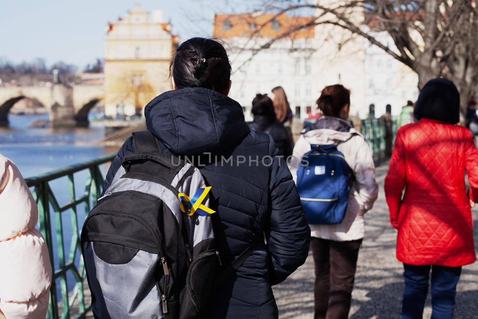 Ukrainian refugees in Europe. Women from Ukraine walk along the street of a European country. Woman with backpack with Ukrainian flag ribbon.
