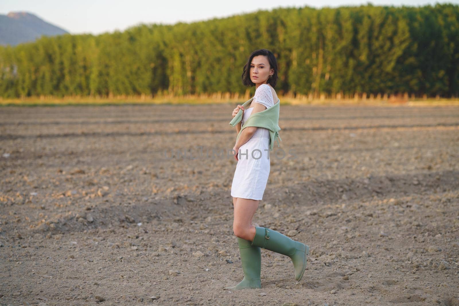 Pretty young Asian woman, walking in the countryside, wearing a white dress and green wellies.