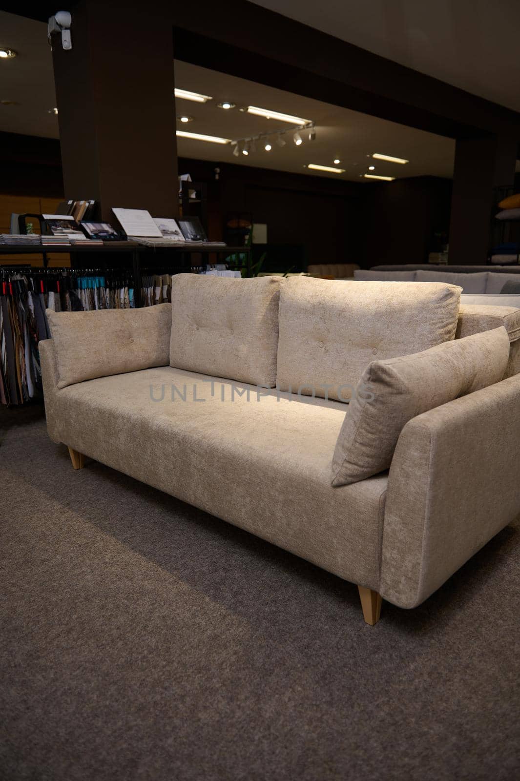 Stylish comfortable sofa with cushions near a stand with fabric samples for upholstery in the showroom of furniture store. Living room furnishing with stylish modern comfortable upholstered furniture by artgf