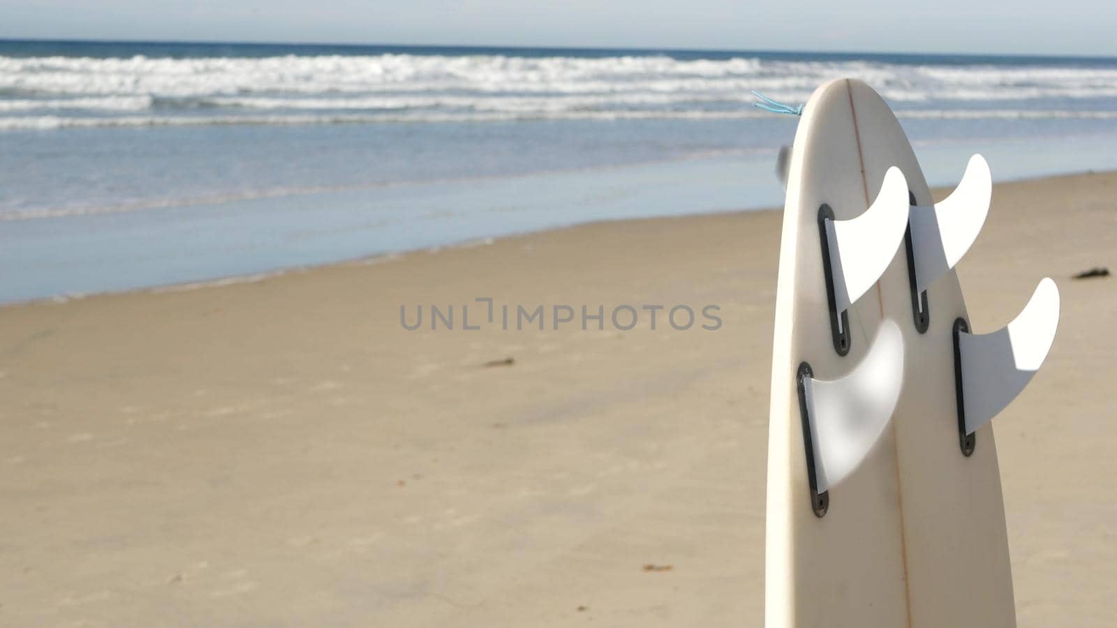 Surfboard for surfing standing on beach sand, California coast, USA. Ocean wave and white surf board or paddleboard. Longboard or sup for watersport by sea water. Summer vacation, sport on shore vibes