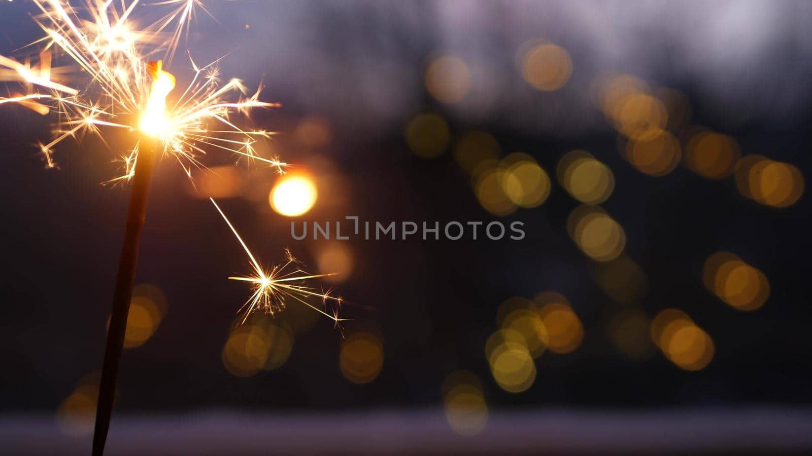 Sparkler firework burning on window, New Year or Christmas bengal lights. Winter Xmas holiday celebration magic, sparkles and golden fire stars light glowing in twilight of night. Garland in bokeh.
