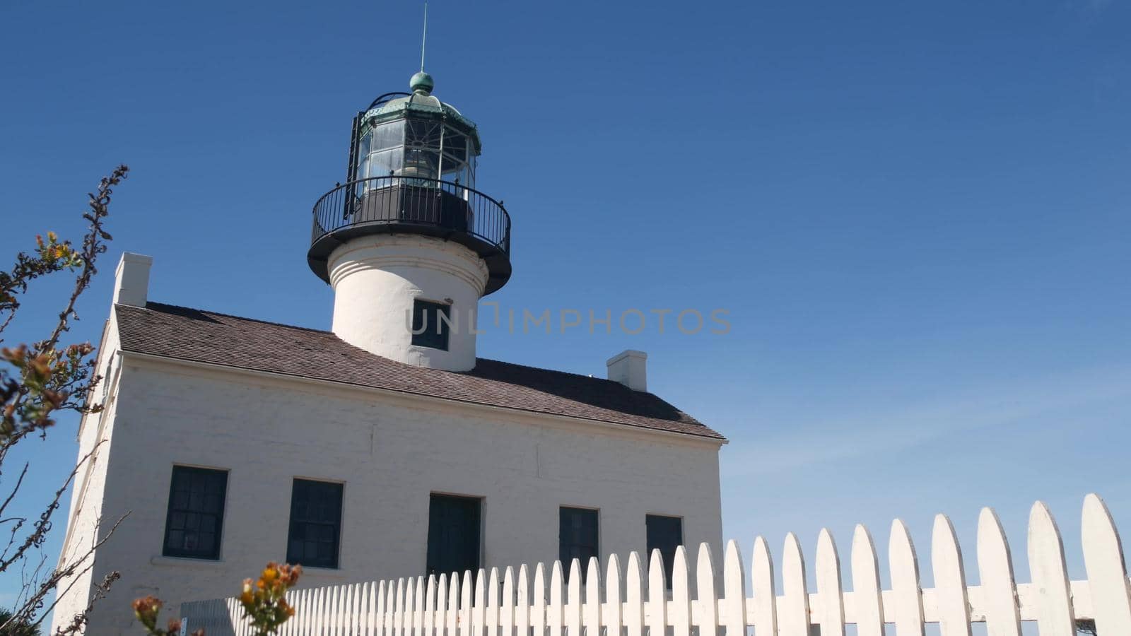 Vintage lighthouse tower, retro light house, old fashioned historic classic white beacon, fresnel lens. Nautical navigational coastal building, picket fence,1855. Point Loma, San Diego, California USA