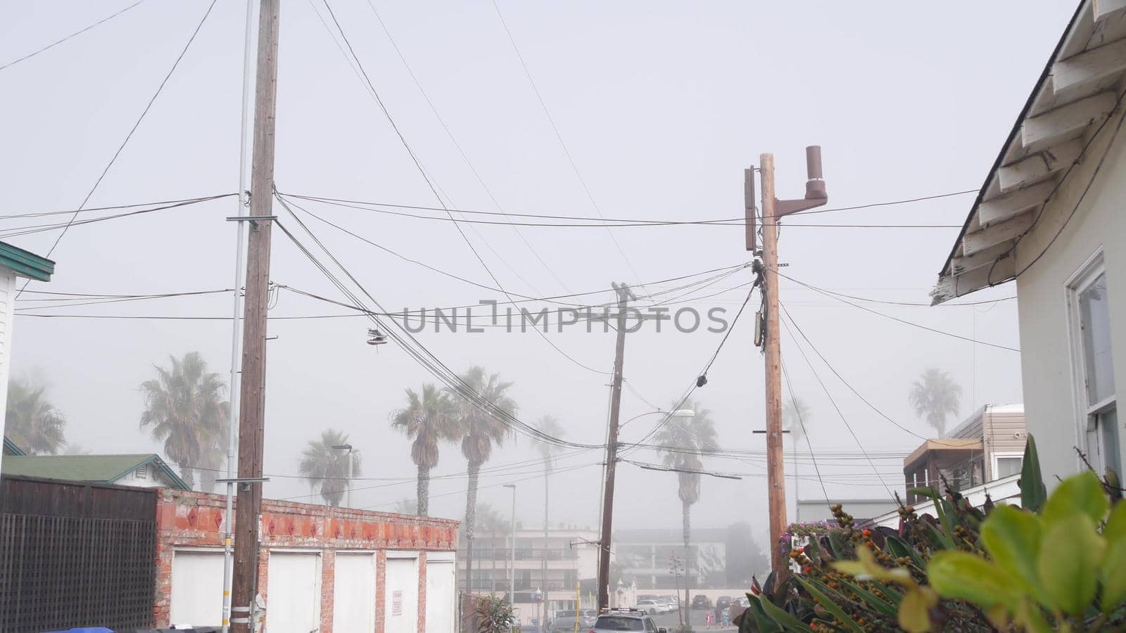 Power lines or wires on poles, foggy city street, California, USA. Cables on high voltage wooden electricity posts or pylons in misty San Diego. Power supply and houses in America. Cloudy weather.