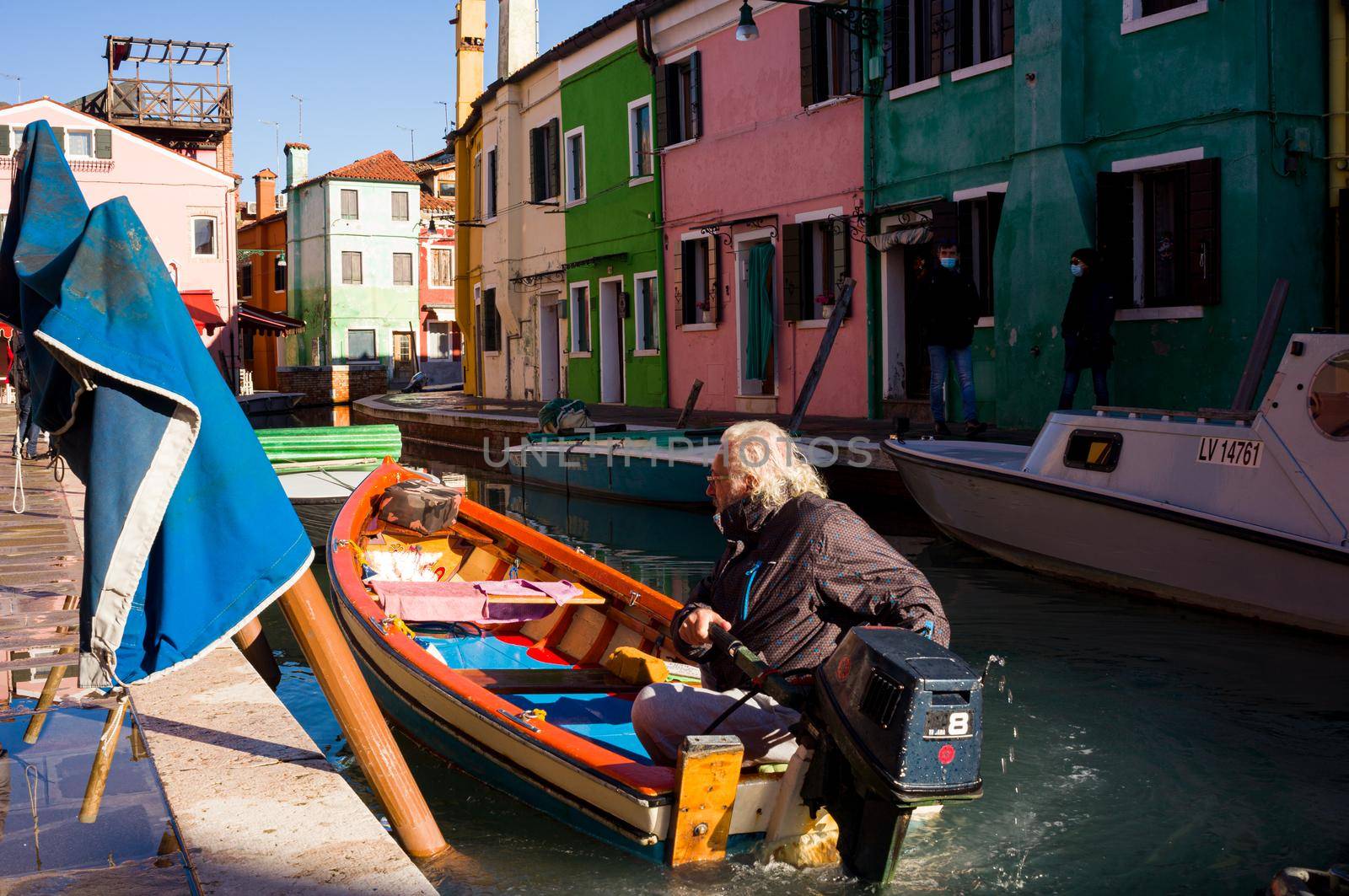 Burano, Italy - January, 06: Italian elderly on his boat navigating in the Burano canal on January 06, 2022