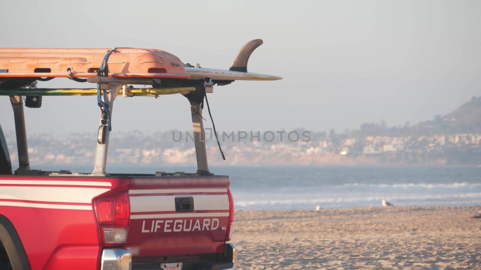Lifeguard red pickup truck, life guard auto on sand, California ocean beach USA. Rescue pick up car on coast for surfing safety, lifesavers 911 vehicle and sea waves of Mission beach near Los Angeles.