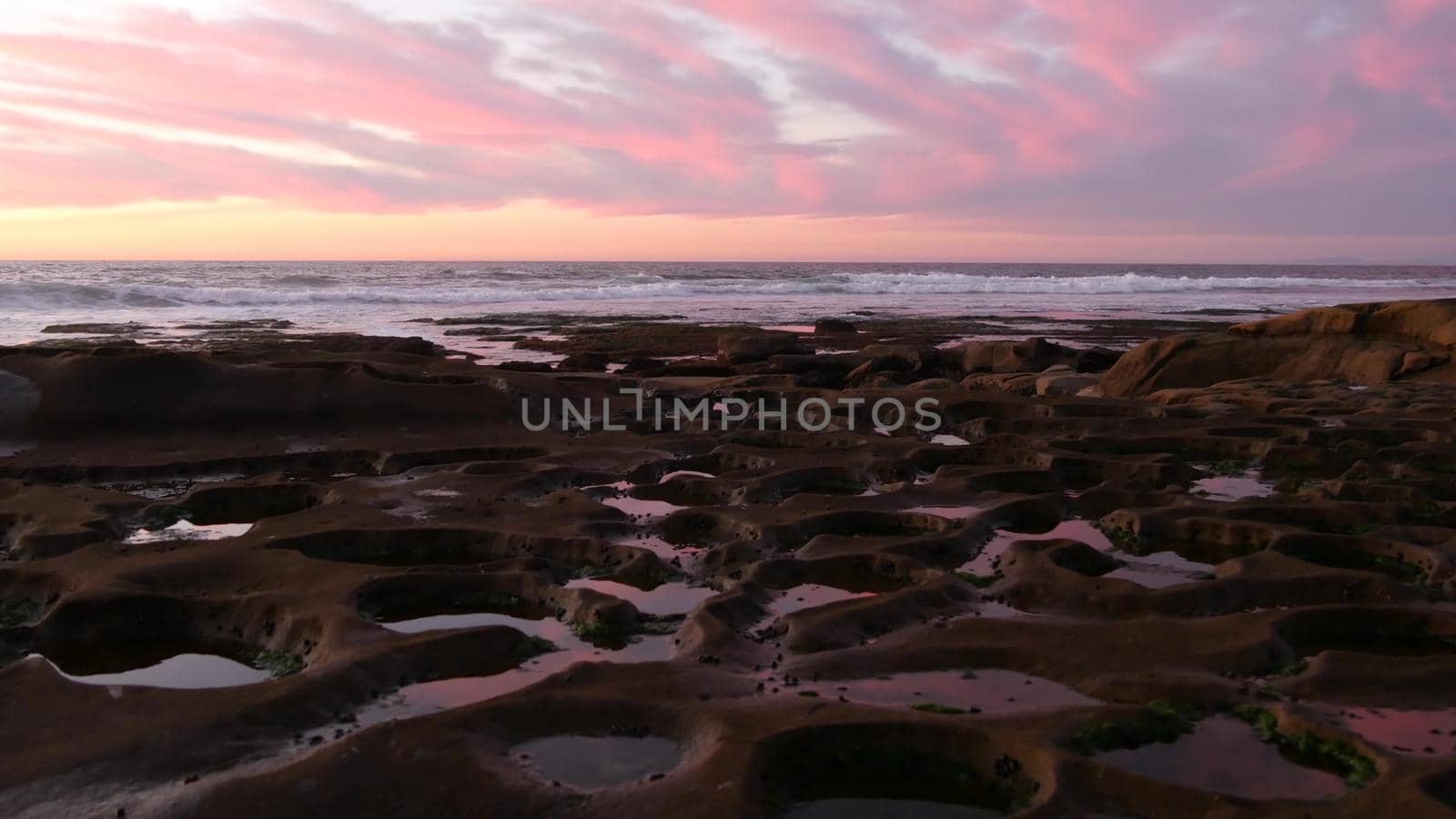 Eroded rock formation, tide pool shape in La Jolla, California coast, USA. Littoral intertidal zone erosion, tidepool relief. Sunset sky reflection in water, cavity, hollows and holes on stone surface