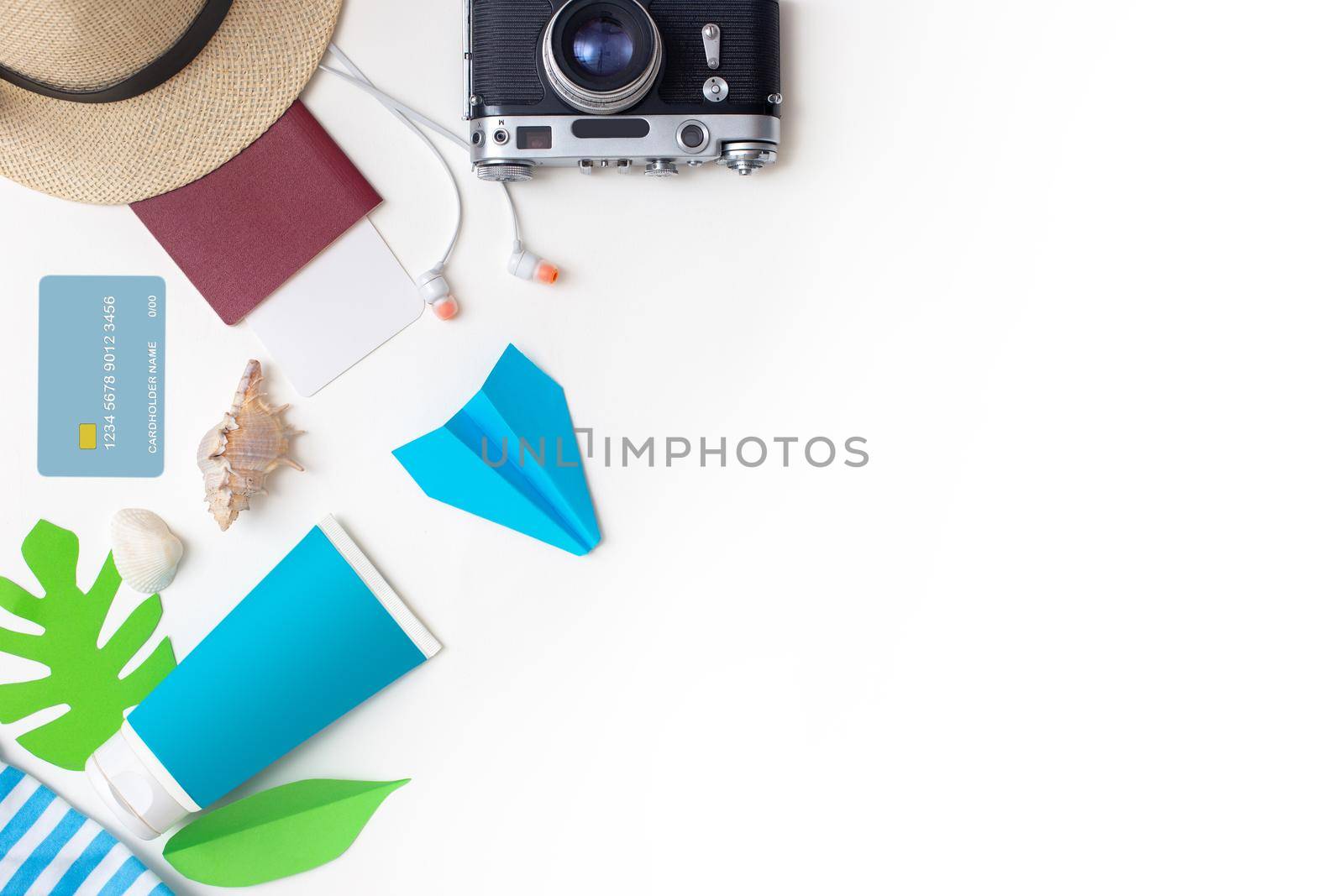 Summer travel accessories set top view: passport, camera, straw hat, sunscreen, headphones, credit card , seashell, paper airplane lies on a white background. Copy space.