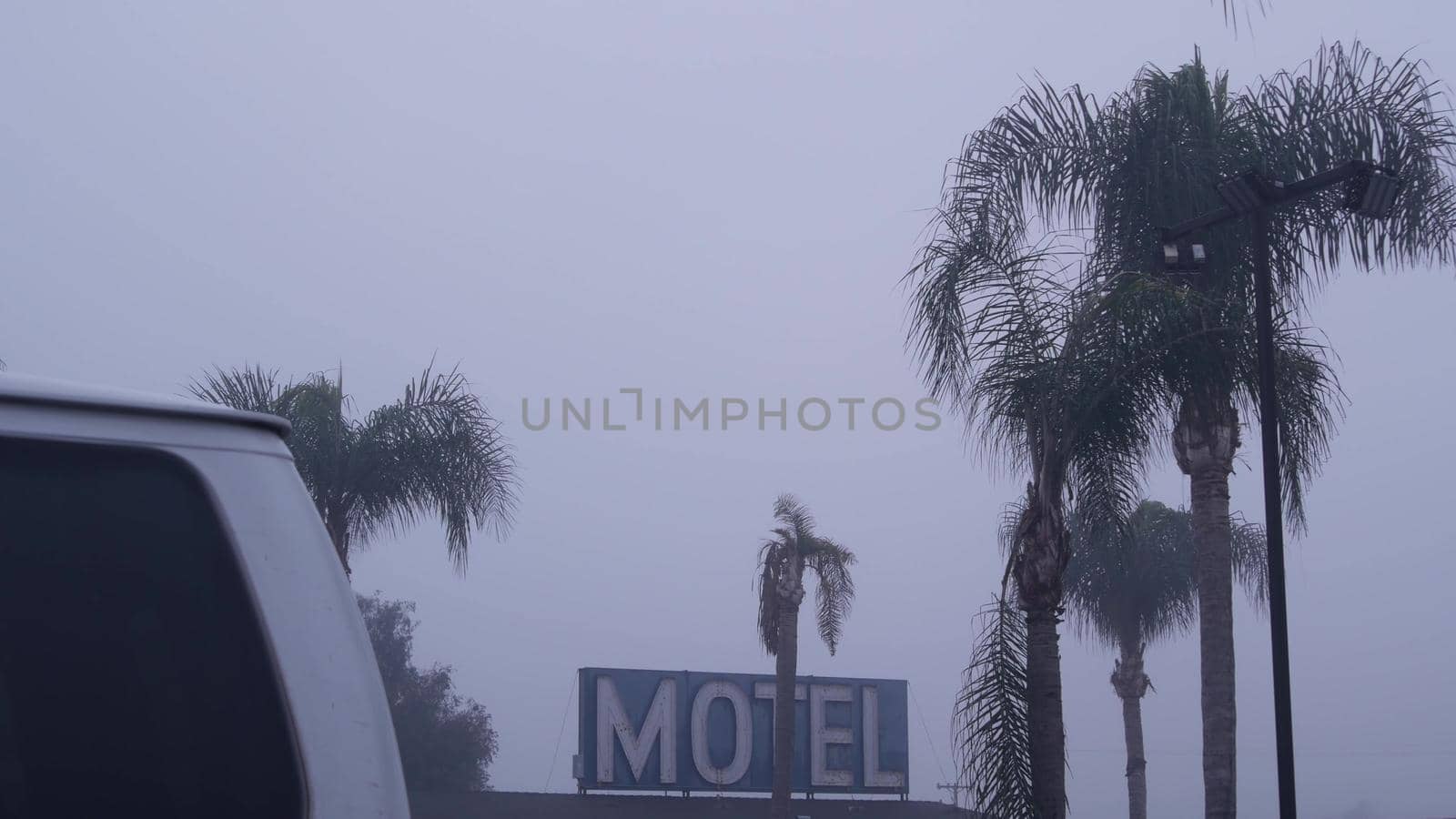 Sign of road motel or hotel, foggy misty weather California, USA. Palm trees. by DogoraSun