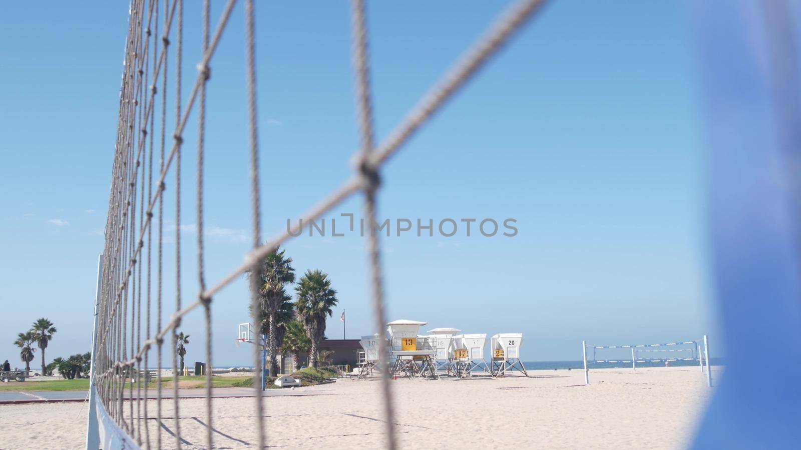 Volley ball net on court for volleyball game on beach, California coast, USA. Sport field or playground for players on sandy ocean shore, lifeguard station and palm trees on Mission beach, San Diego.