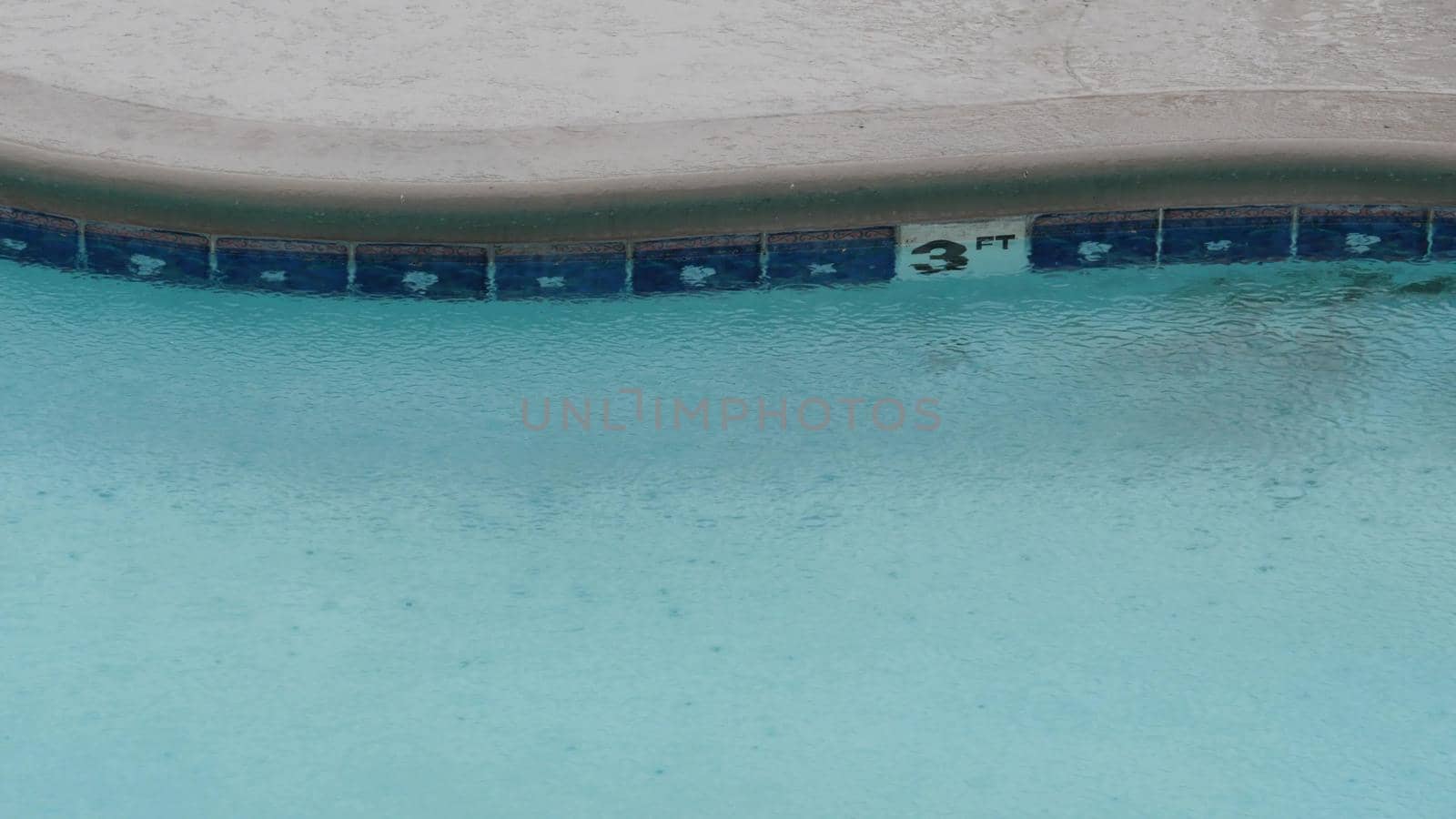 Rain drops falling on water of swimming pool, rainy in California motel or hotel by DogoraSun