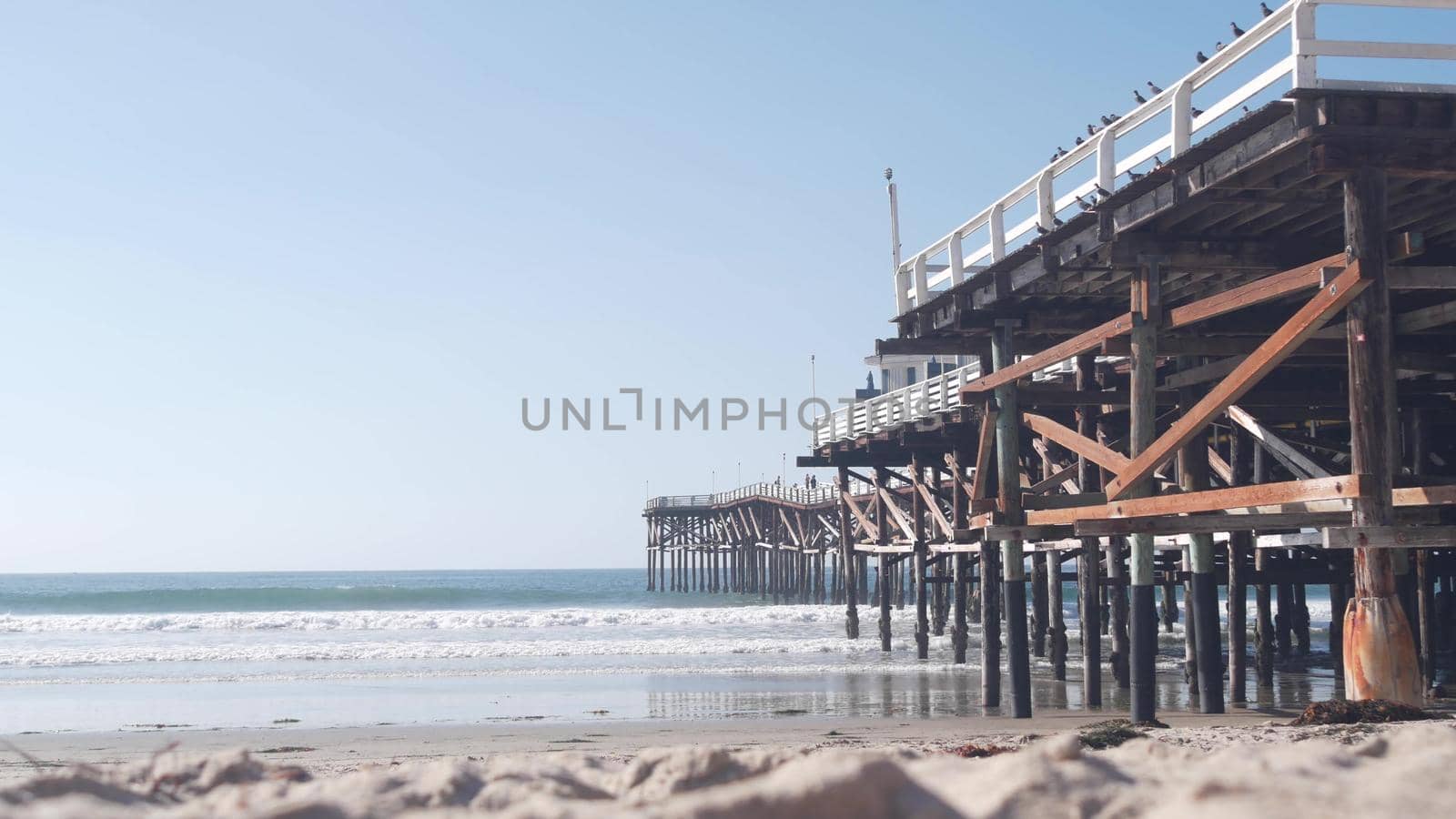 Below wooden Crystal pier on piles, ocean beach water waves, California USA. by DogoraSun