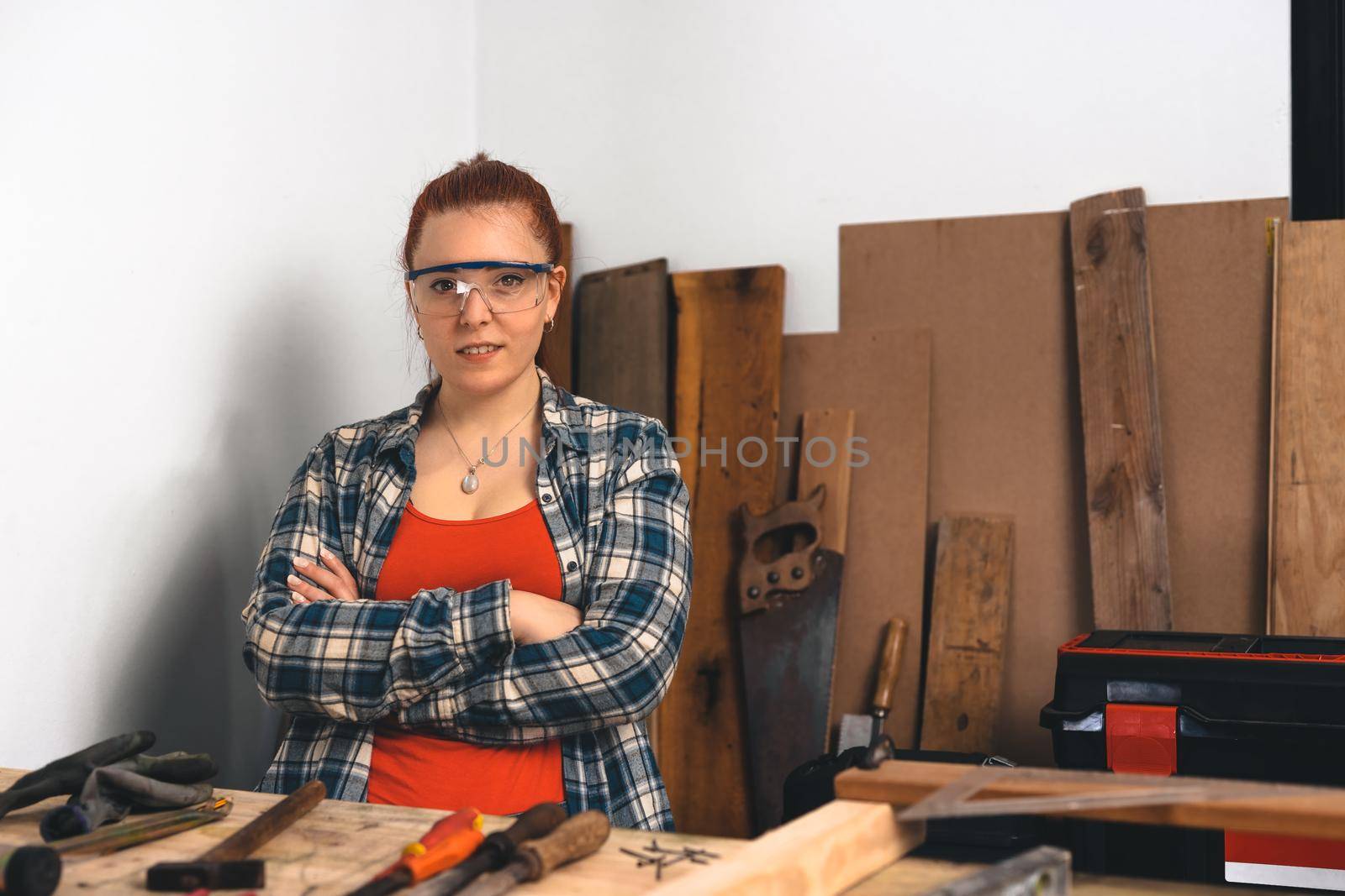 Portrait of a young red-haired female carpenter in her small carpentry workshop. Copy space on the right by CatPhotography