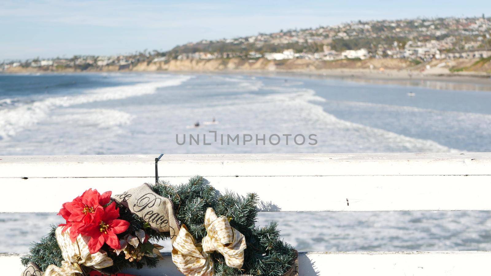 Christmas wreath on pier, New Year on ocean coast, California beach at Xmas. Decor from pine or fir tree for winter holidays over sea in USA. Festive decoration over summer seascape in December.