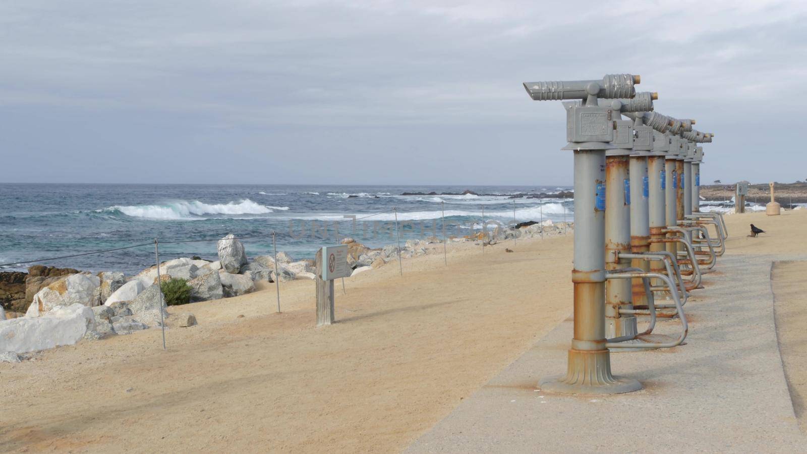 Stationary binoculars, telescope, tower viewer or scope, ocean waves on rocky craggy beach. Magnifier or spyglass row, 17-mile drive tourist viewpoint, Monterey, California USA. Bird Rock Vista Point.
