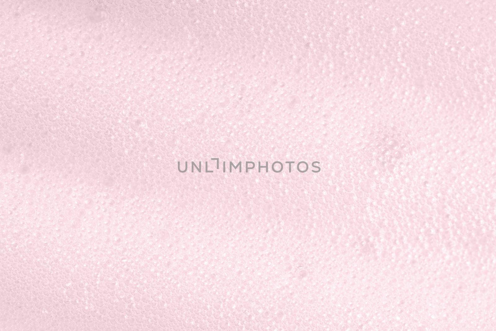 Pink foam macro background with bubbles. Soapy surface closeup. Foamy cleansing skin care product texture from soap, detergent, shampoo, shaving foam or cleanser. Laundry spume