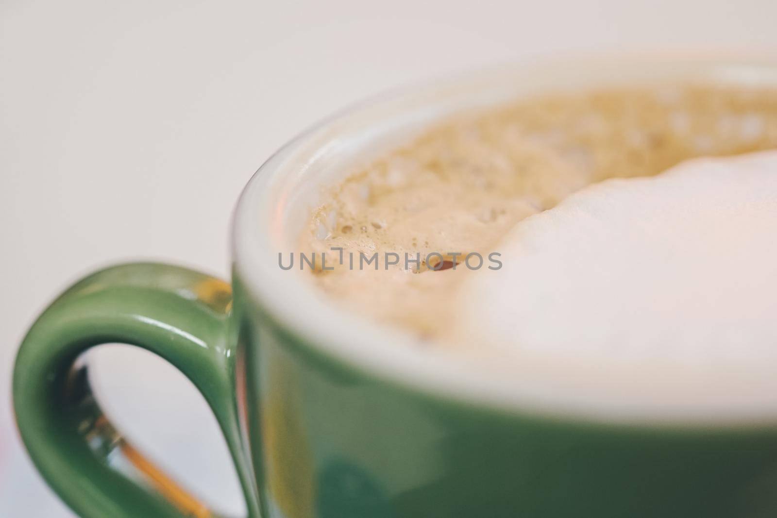 Coffee in green cappuccino ceramic cup with frothy foam, latte capuccino mug closeup. Hot coffee latte in jade color porcelain cup on table in cafe close up. Selective focus