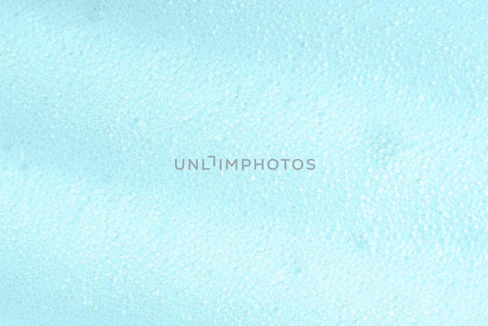 Blue soapy surface closeup. Foamy cleansing skin care product texture from soap, shaving foam or cleanser. Foam macro background with bubbles by photolime