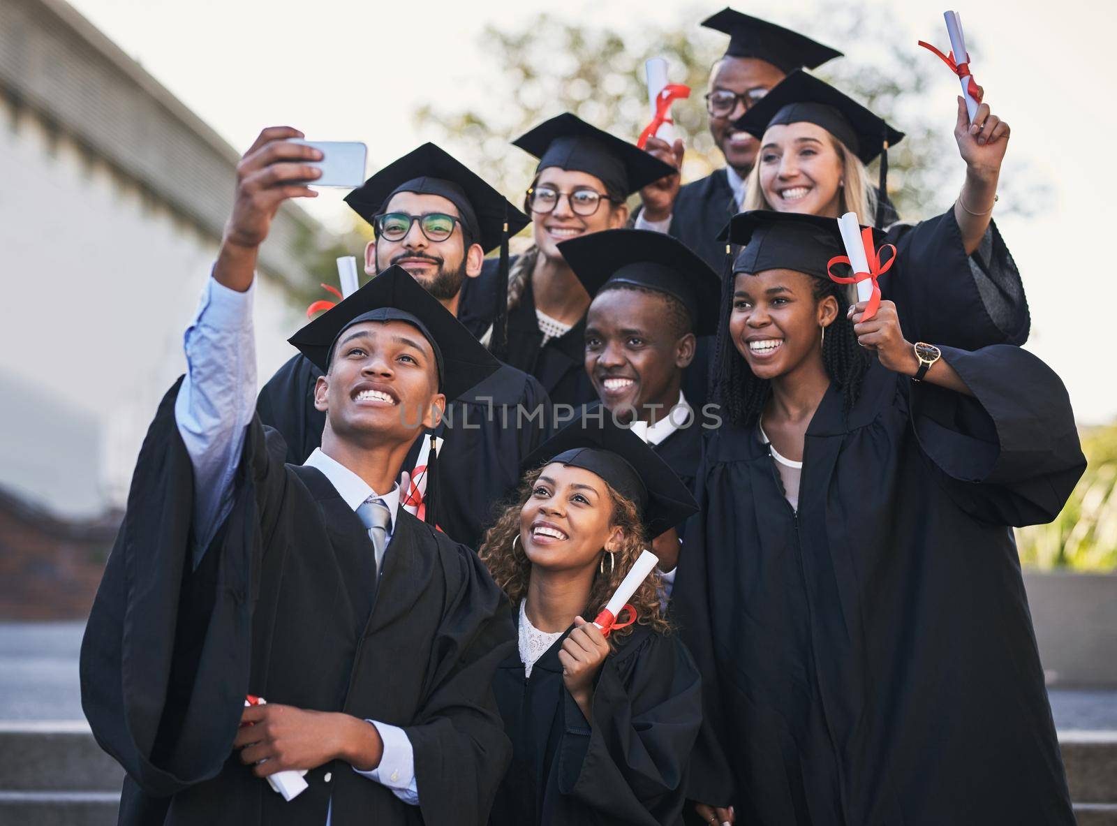 We earned our bragging rights. Shot of a group of students taking a selfie on graduation day. by YuriArcurs