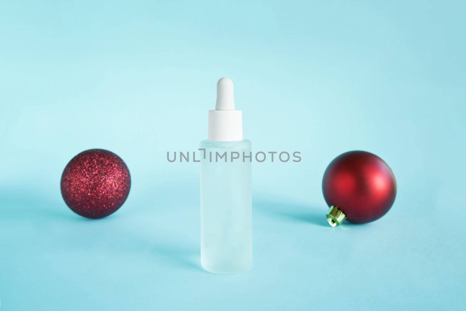 Serum oil with collagen and peptide in white transparent bottle with dropper on blue backdrop and red baubles. Skincare beauty treatment medical skincare mockup packaging liquid cosmetic by photolime