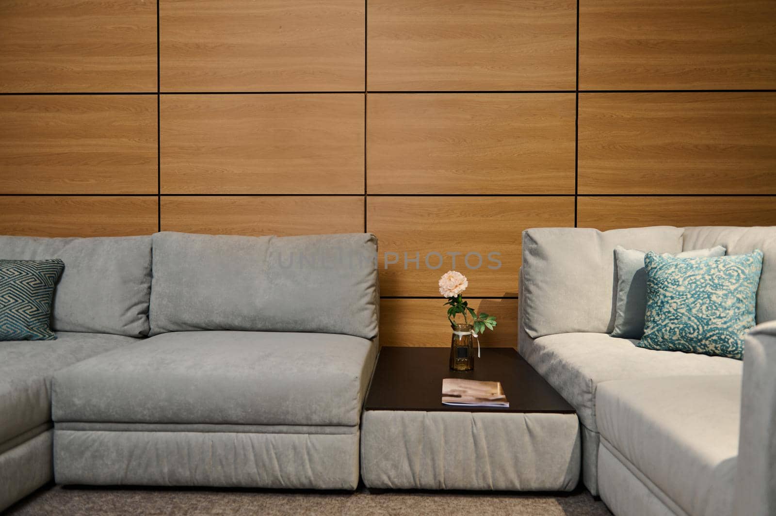 Modern stylish comfy soft upholstered gray sofa with green pastel pillows and a journal table with a rose in the vase in the showroom of a furniture store