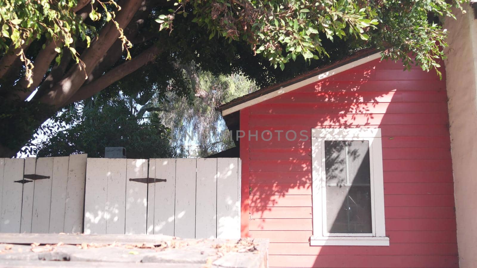 Red wooden rural ranch house, rustic building exterior, window and gate under tree, California, USA. Provincial homestead architecture, facade of retro farm in country village. Countryside dwelling.