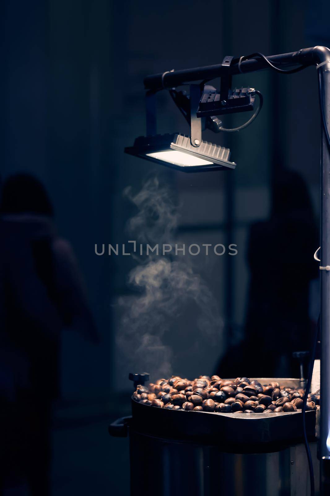 Grillled chestnuts in the night city under street lamp. Fried chestnut vendor, street food. Milan, Italy - December 25, 2019