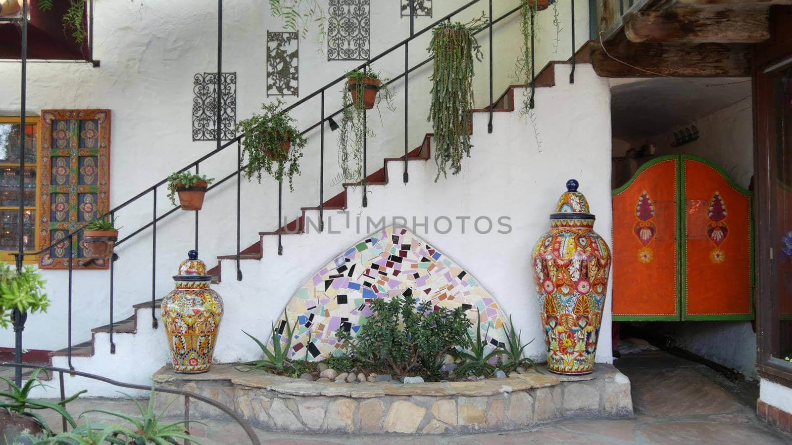 Mexican garden design in front yard, colorful ceramic painted decor, window, stairs and succulent plants in clay flower pots. Ethnic latin white house exterior, rural patio or terrace in latino style.