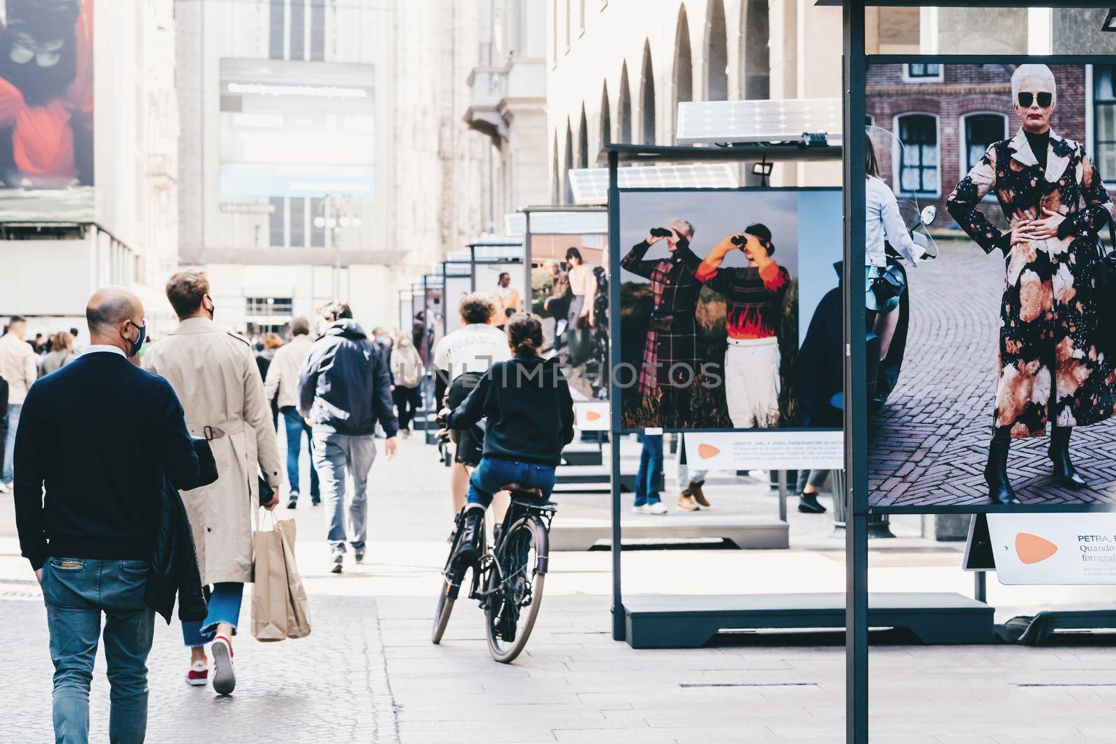 People in masks walking street in downtown of Milan, commuting, cycling. Modern fashion photography street exhibition using solar batteries by photolime