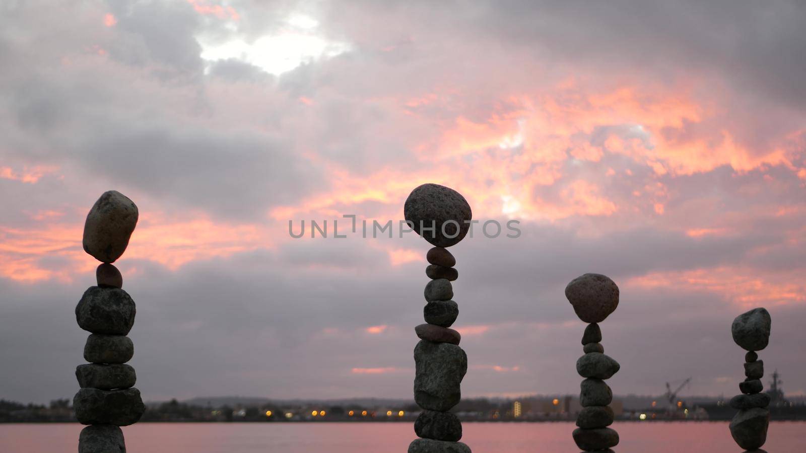 Rock balancing against cloudy dramatic sky on sunset. Stack of stones in balance, stable pyramid in pink twilight of evening. Cloudscape at sundown time by sea ocean water. Buddhism concept.