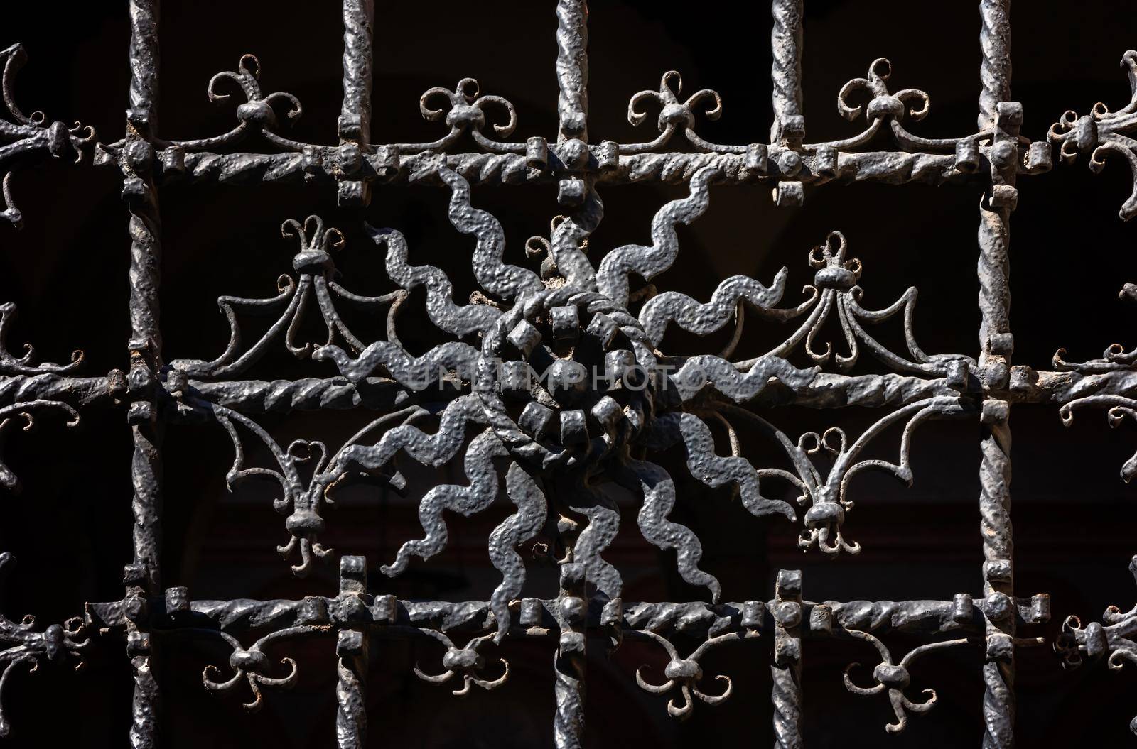 Ornate curly metal grid on religious building in Milan on sunny day. Vintage picturesque window in european city. European architecture by photolime