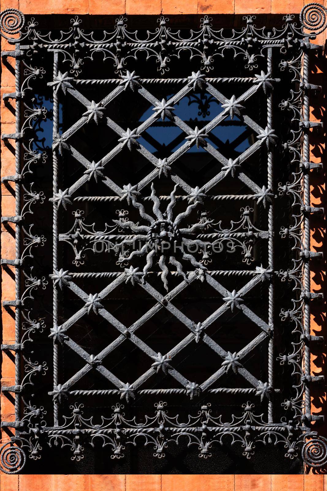 Window with ornate curly metal grid on religious building in Milan on sunny day. by photolime