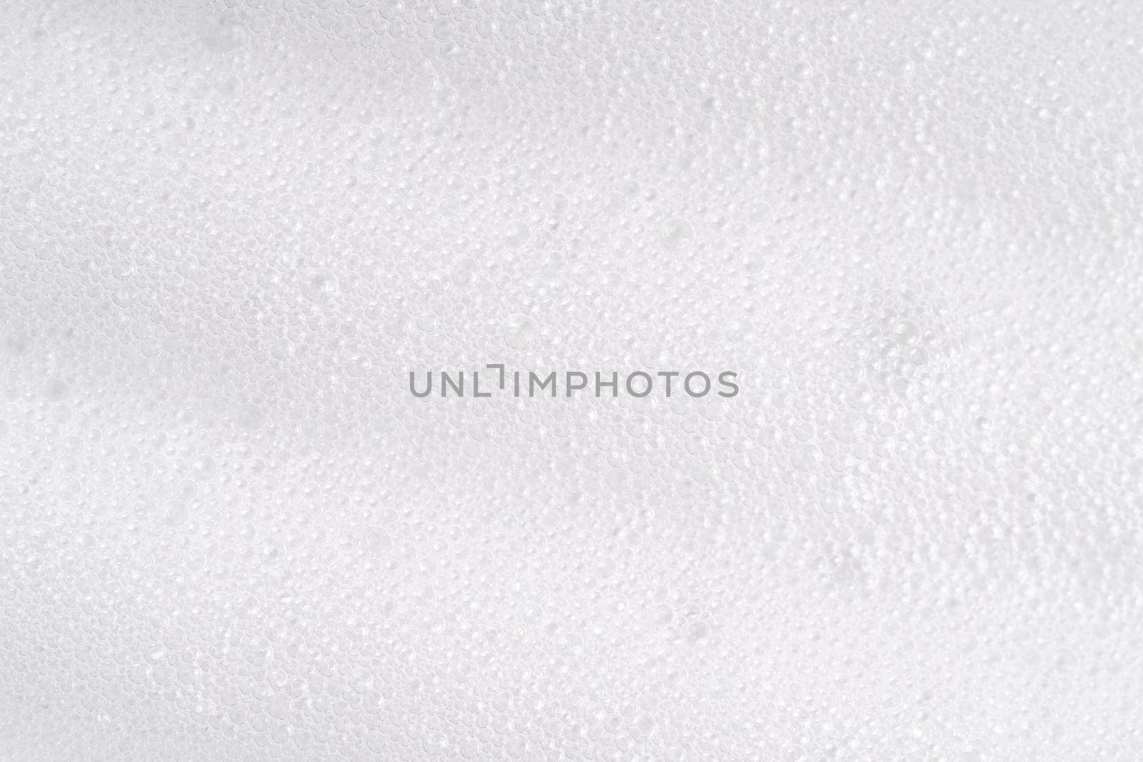 White foamy cleansing skin care product texture from soap, detergent, shampoo, shaving foam or cleanser. Soapy surface closeup. Foam macro background with bubbles. Beer drink backdrop, laundry spume