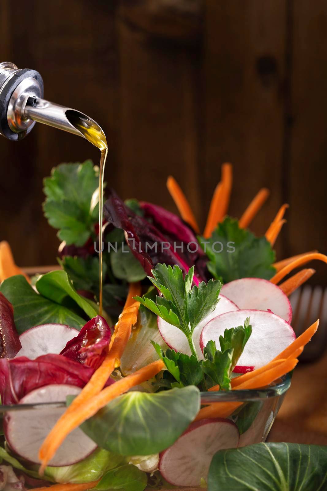 Vegetable salad with olive oil dressing on rustic background. Olive oil stream and healthy fresh vegetable salad. Olive oil pouring into bowl of greenery. Copy space for text