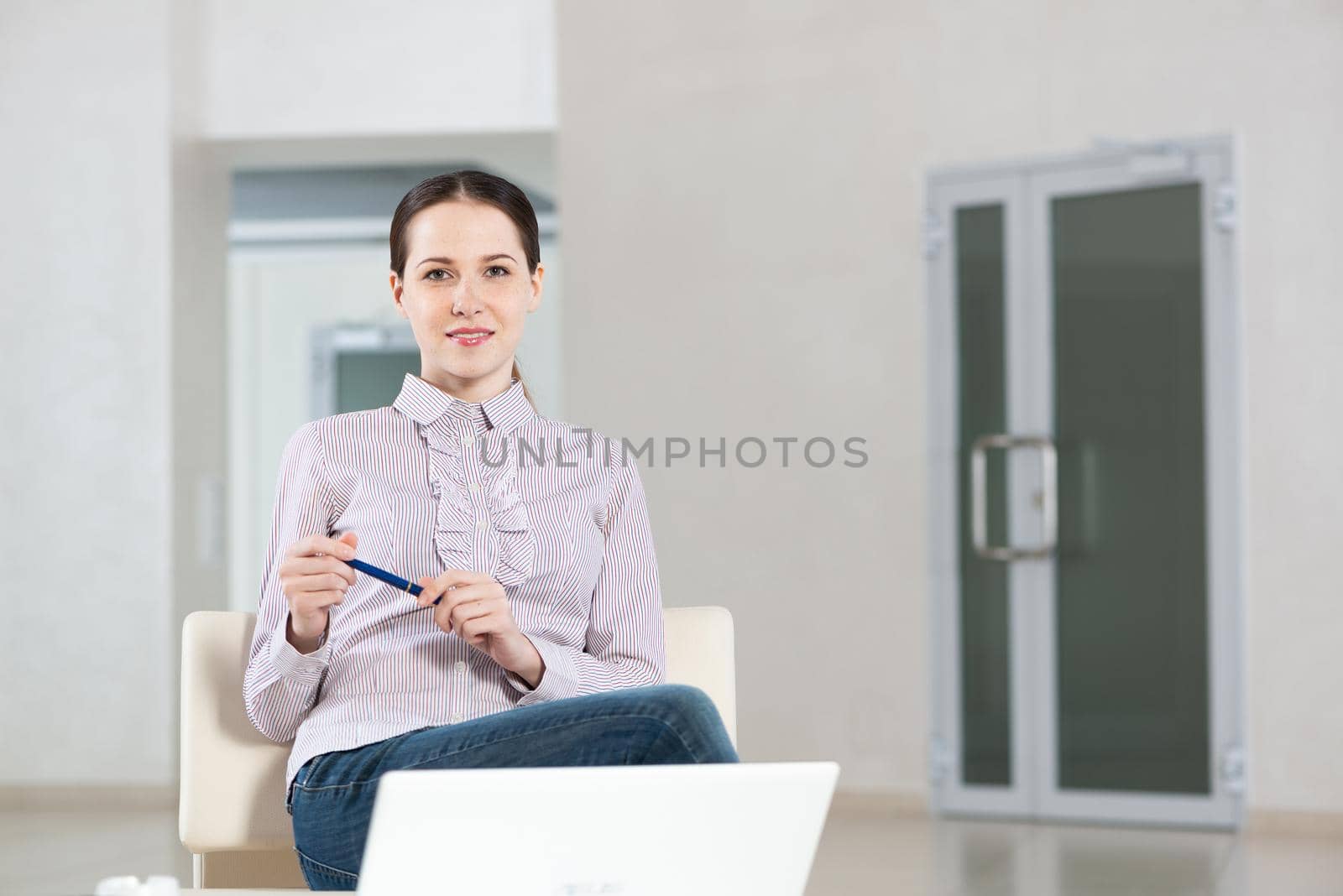 Portrait of a young attractive woman in a light chair, in an office space