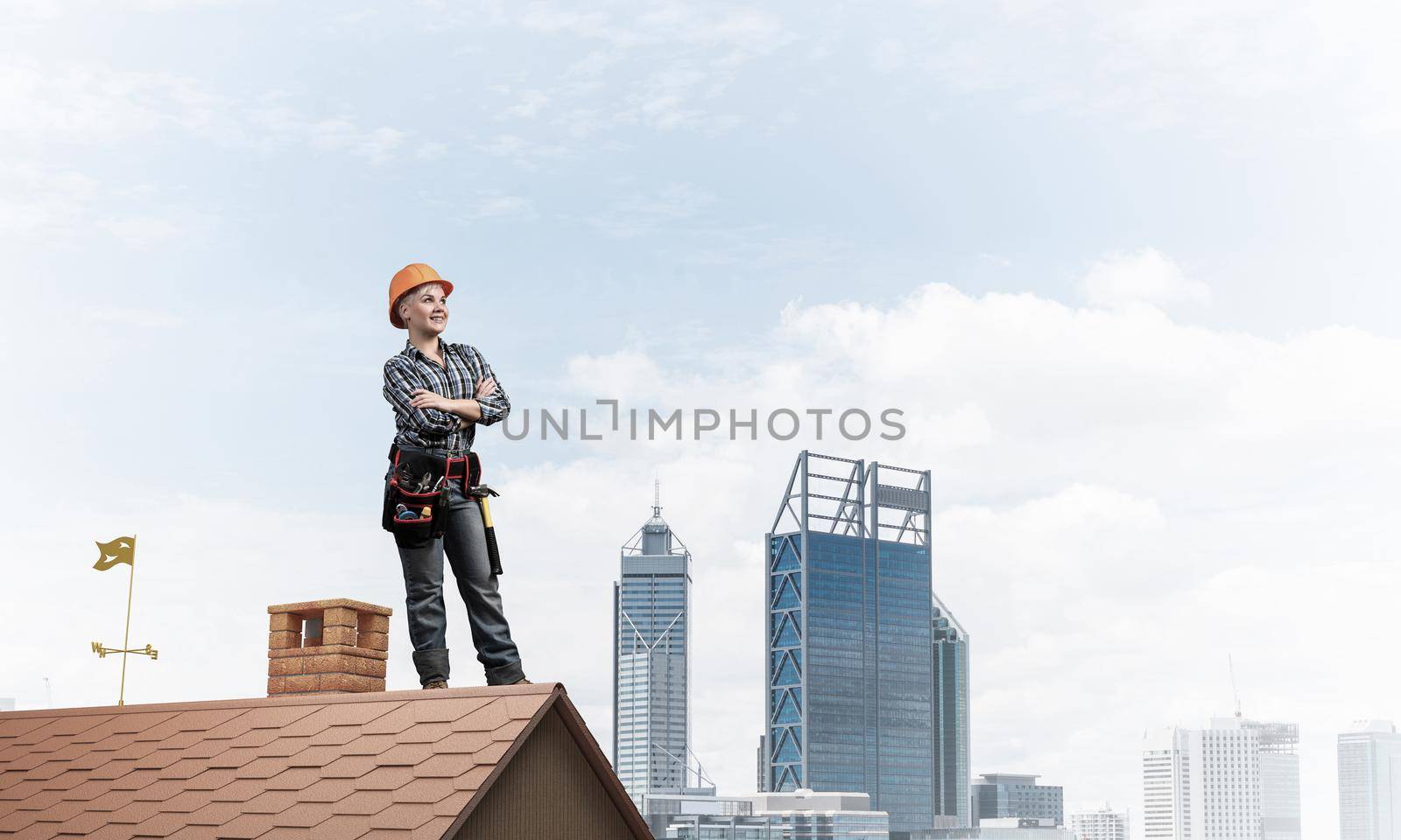 Attractive female construction worker in hardhat standing with folded arms. Confident young woman in checkered blue shirt standing on brick roof of building. Professional perspective and motivation