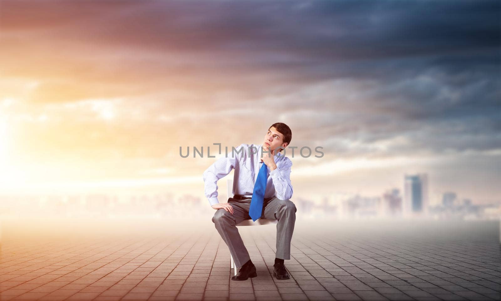 young businessman sits on an office chair, thoughtful and looking up