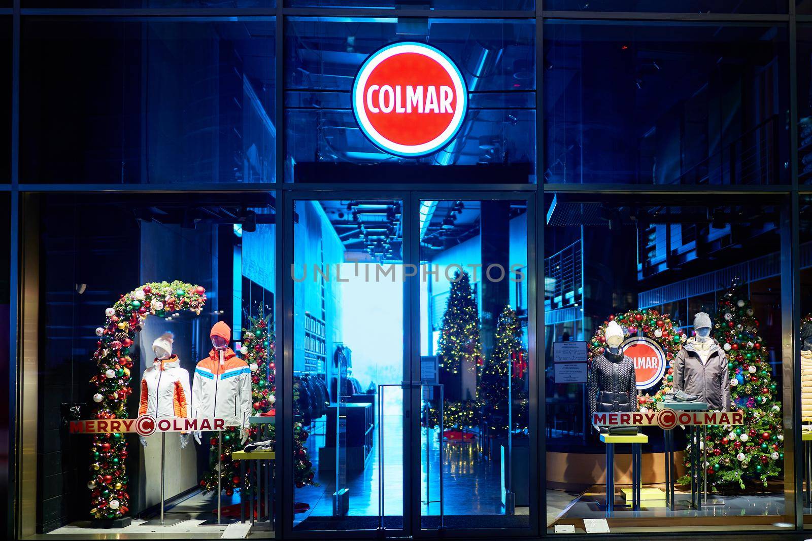 Colmar logo and showcase of the store at night with christmas decoration. Four mannequins standing in store window display. Milan, Italy - 17.12.2020 by photolime