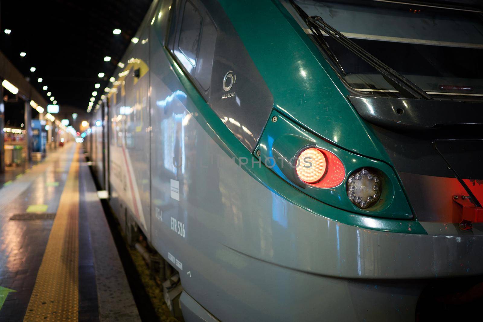 European railway train station platform with no people at night, train arriving at rail way platform, industrial landscape, blurred background. Milan, Italy - December, 15, 2020