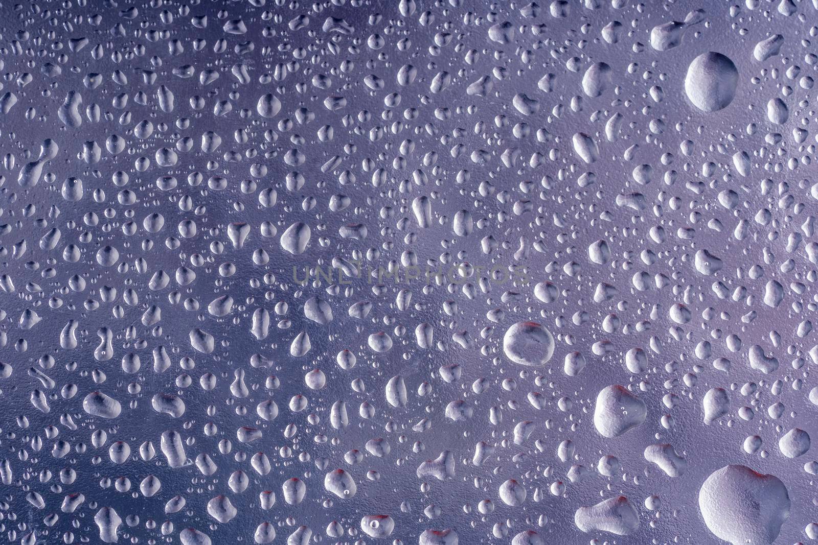 Water drops on glass. Small transparent droplets on the window. Liquid parts on grey surface. Rainy background, autumn season backdrop, abstract textured wallpaper. Dark cold blue tone. Wet glass