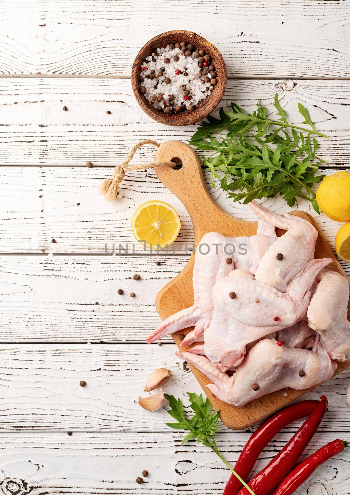 Sliced chicken wings with skin on a cutting board. White wooden background with copy space
