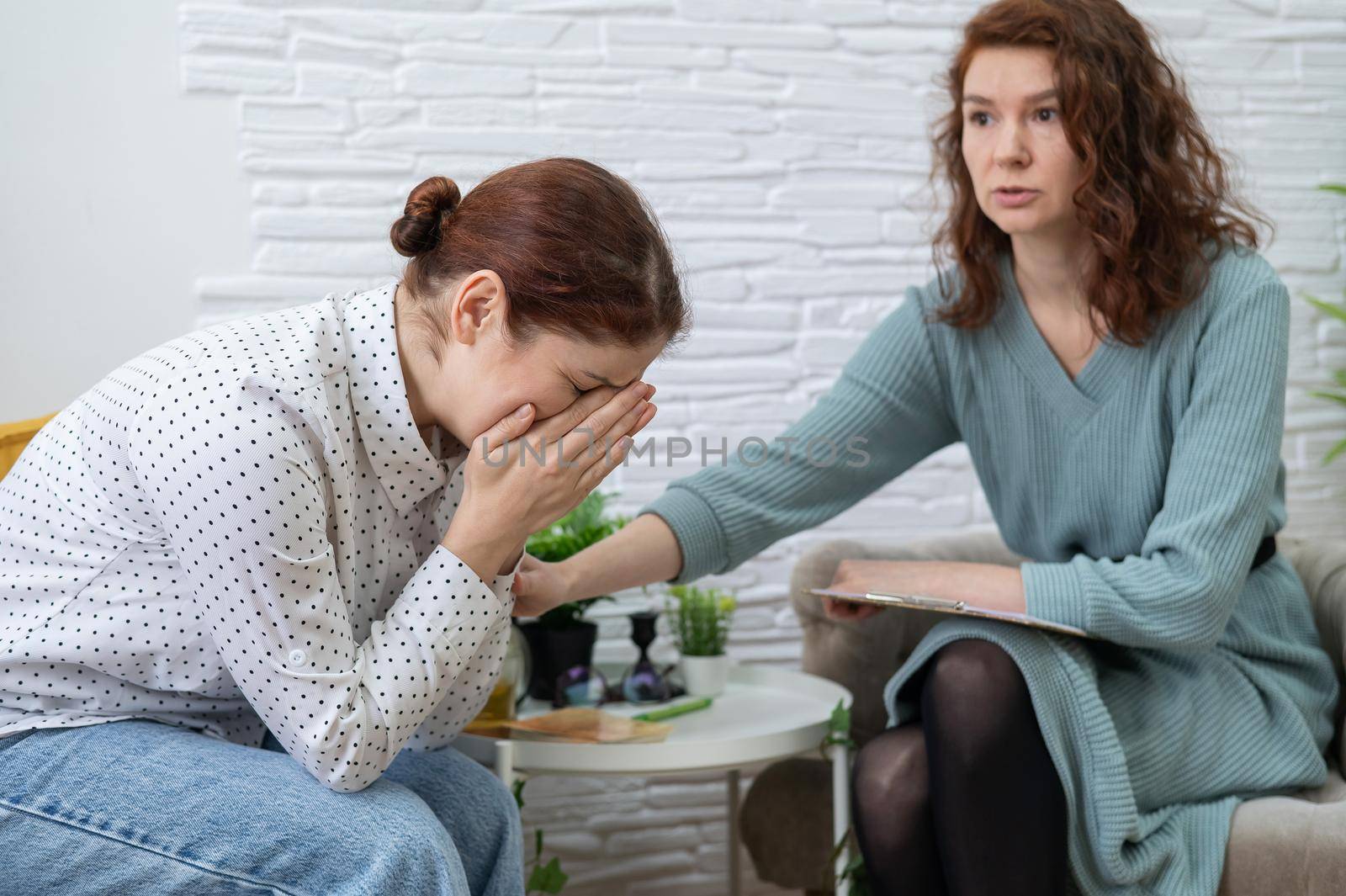Caucasian woman crying at psychotherapy session. The female doctor calms the patient and holds her hand