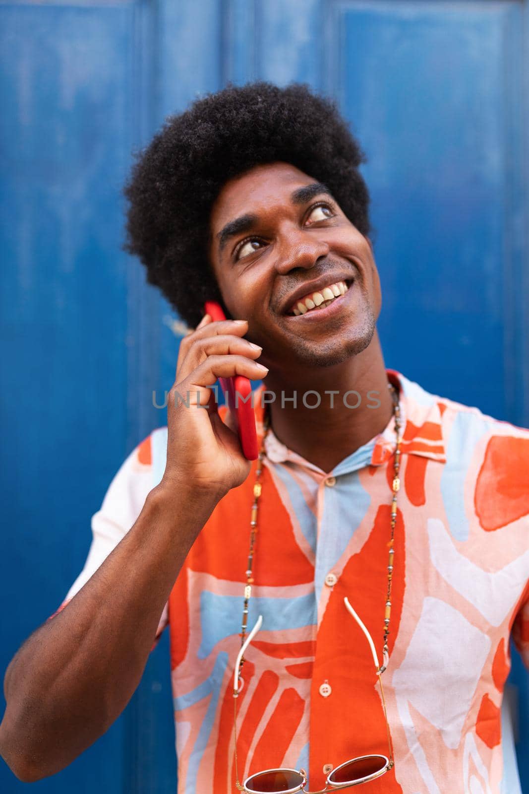 Vertical portrait of happy black man talking on the phone. African American man using mobile phone in the street. by Hoverstock