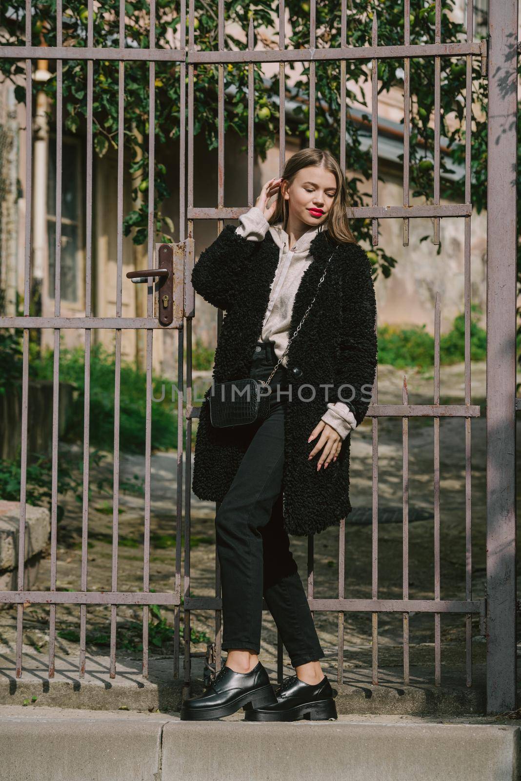 Fashion photo of young woman in black fur coat, jeanse and shoes at city street. beige jacket with a hood