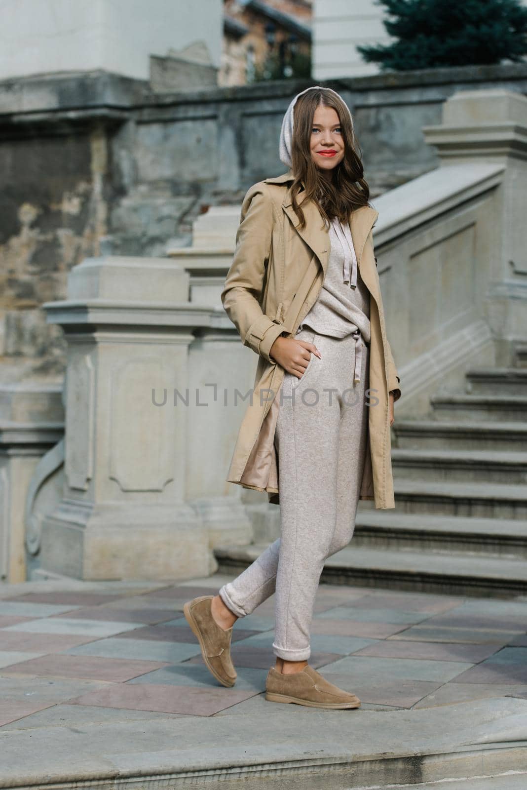 Portrait of fashionable women in beige sports suit, trench coat and stylish suede loafer posing on the stone stairs. street look fashion