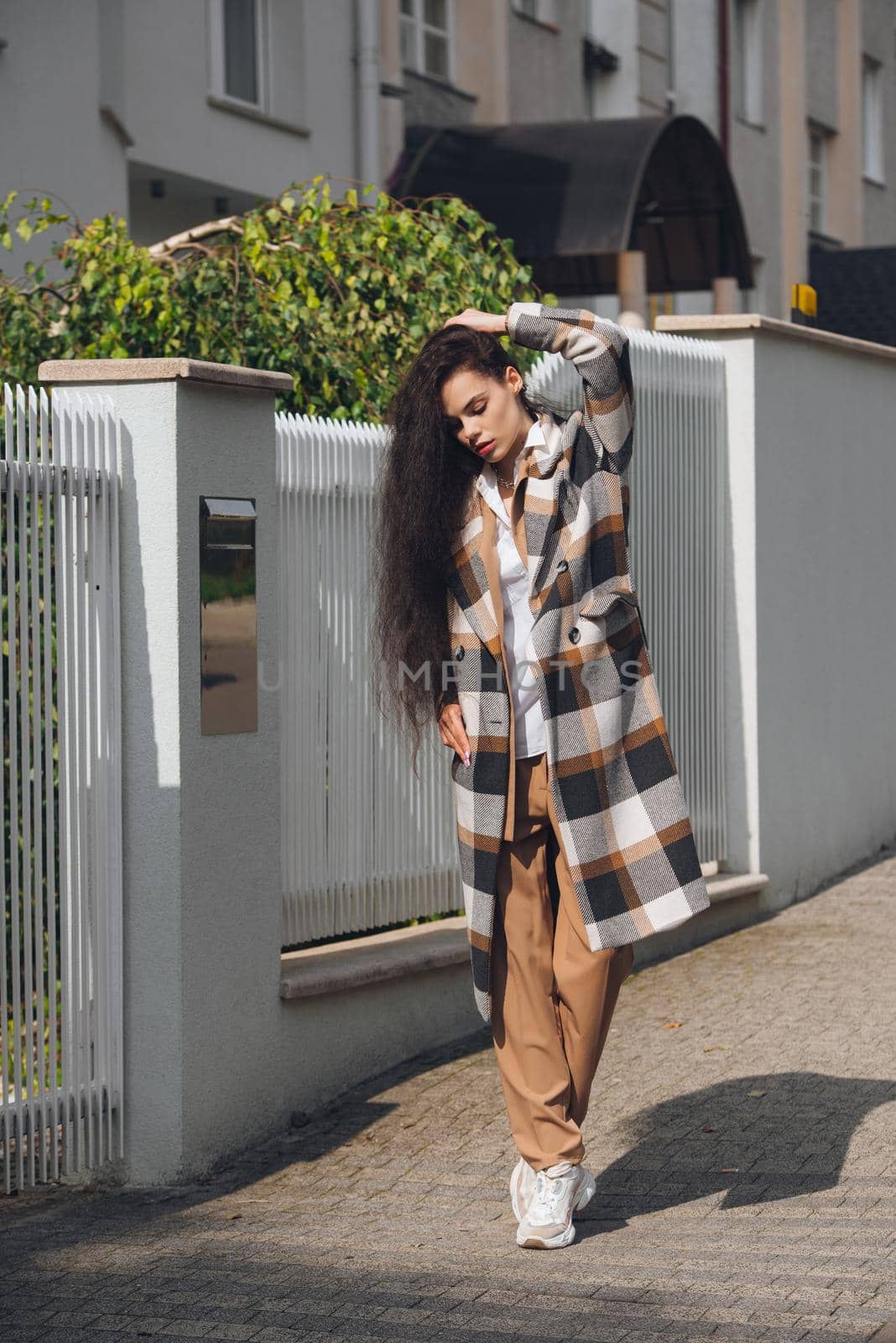 Closeup portrait of young beautiful fashionable woman wearing checkered long coat, beige pants and white blouse . Lady posing on city street. by Ashtray25