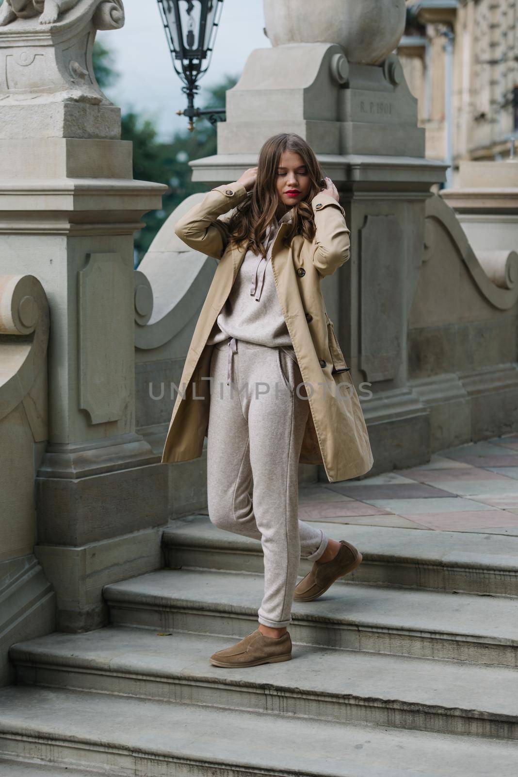 Portrait of fashionable women in beige sports suit, trench coat and stylish suede loafer posing on the stone stairs by Ashtray25